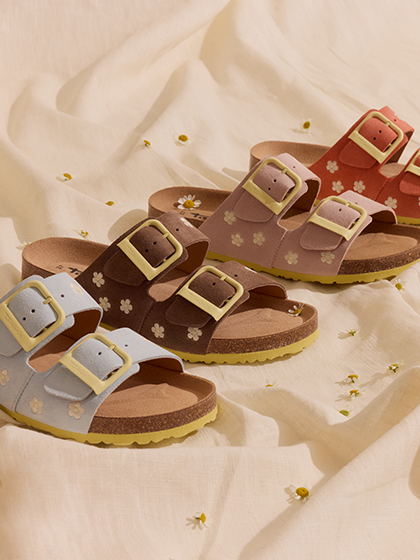 Quattro sandali con fibbie in blu, marrone, rosa e rosso con motivo floreale su tessuto chiaro con piccole margherite.