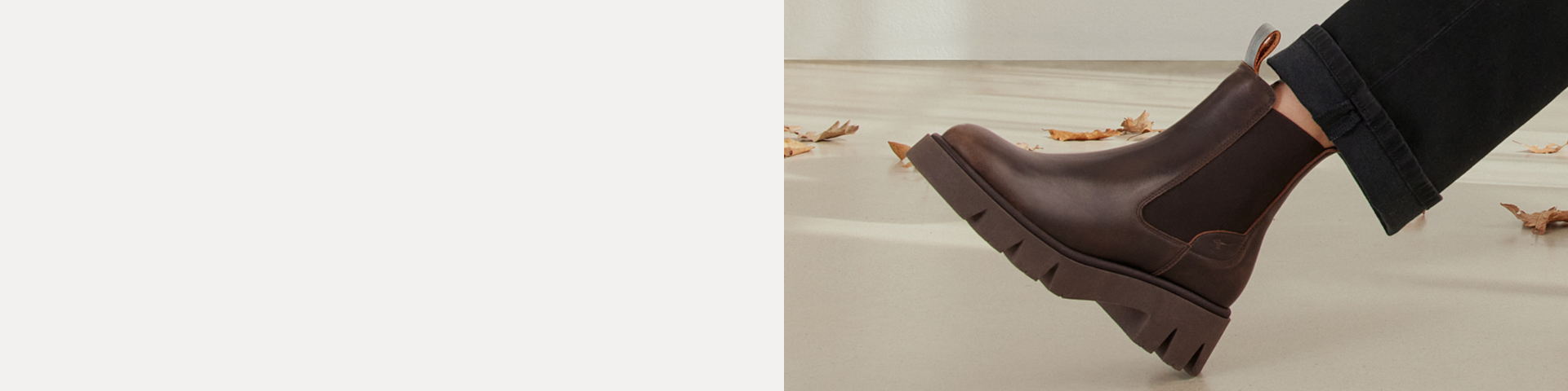 Brown Chelsea boot with a chunky treaded sole, worn with black trousers, on a light floor with autumn leaves.