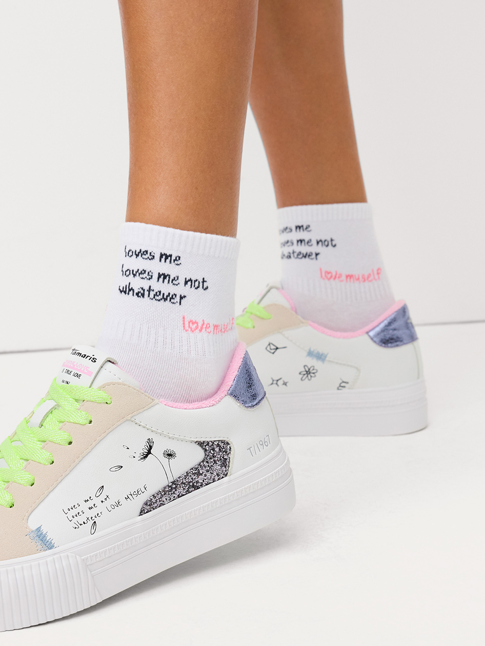 Baskets Tamaris blanches avec lacets de couleur n&eacute;on et d&eacute;tails scintillants, associ&eacute;es &agrave; des chaussettes blanches avec l'inscription &laquo; love myself &raquo;.