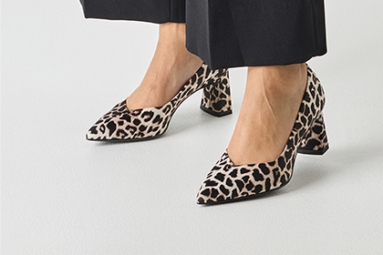 Elegantn&iacute; lodičky s leopard&iacute;m vzorem a &scaron;pičatou &scaron;pičkou, zkombinovan&eacute; s čern&yacute;mi kalhotami na b&iacute;l&eacute;m pozad&iacute;.