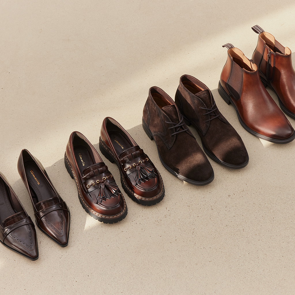Vier paar bruine schoenen: pumps, loafers met kwastjes, veterschoenen/laarzen en Chelsea‑boots op een lichte ondergrond.