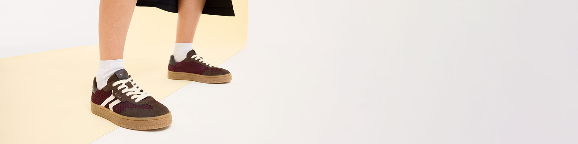 Vinrøde sneakers med hvide striber og gummisål, båret med hvide sokker foran en lys baggrund