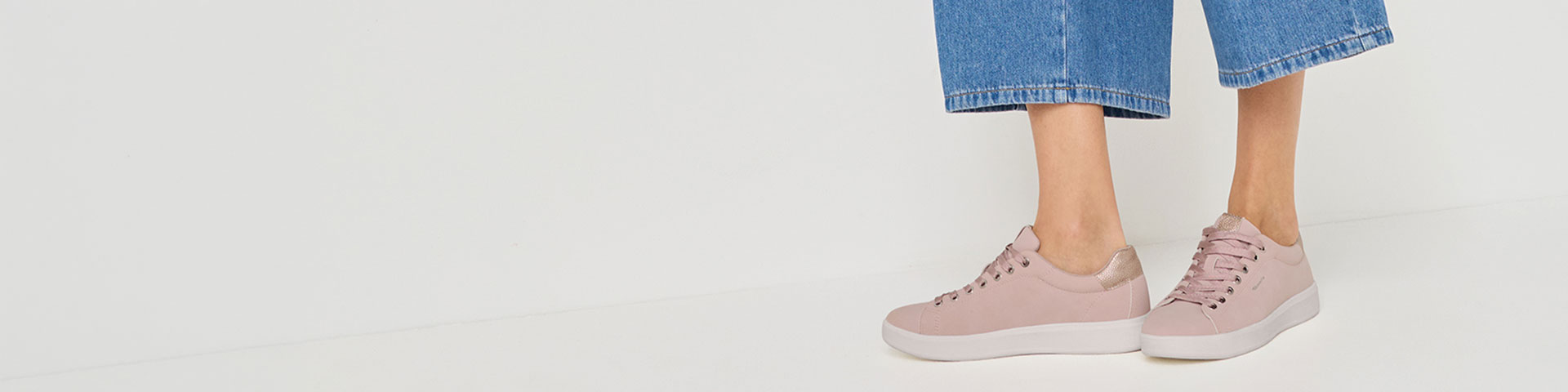 Sneakers rosa con suola bianca, abbinate a jeans blu su sfondo bianco.