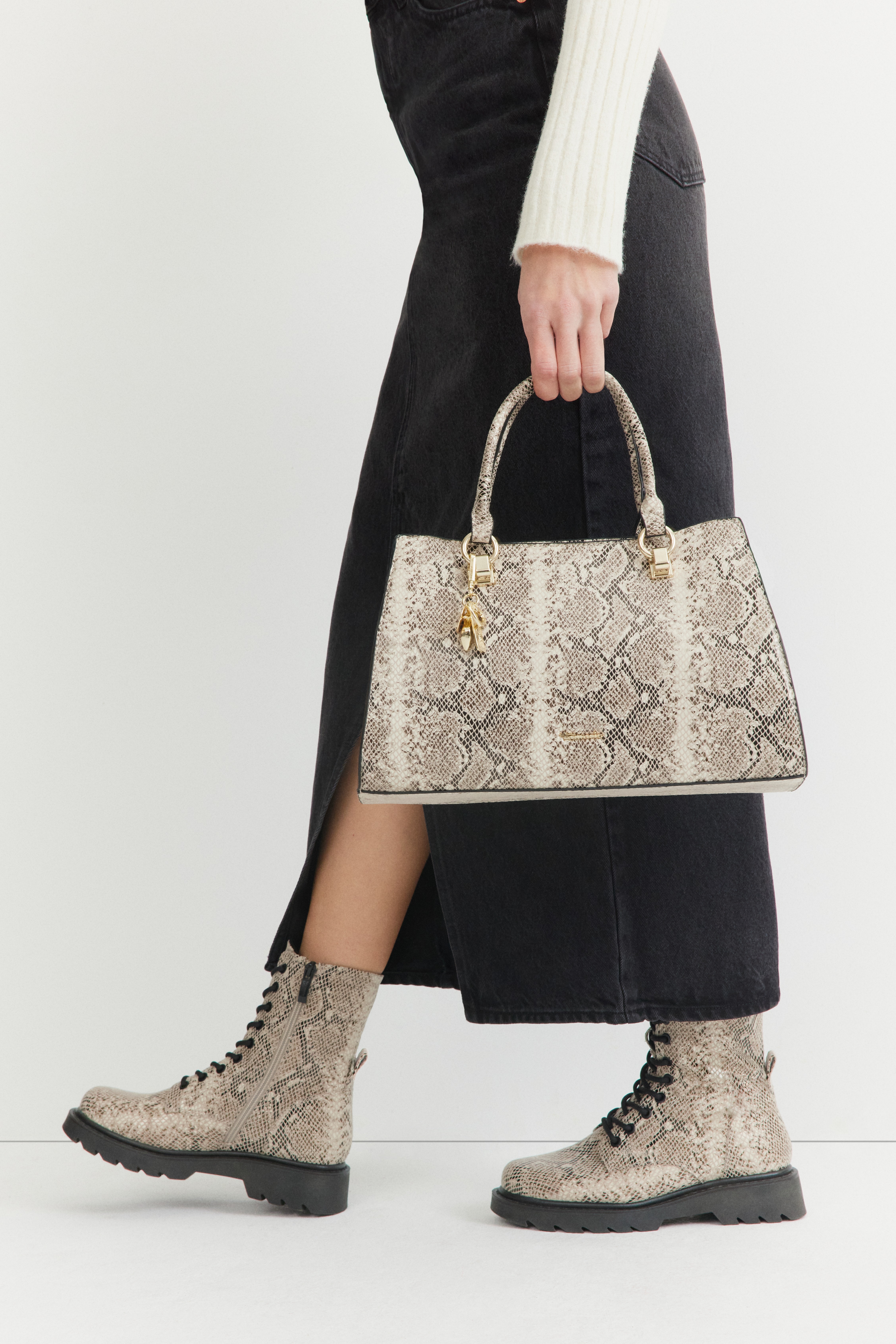 Person wearing a white knitted dress carries a handbag and ankle boots with a snake pattern, perfectly coordinated. 