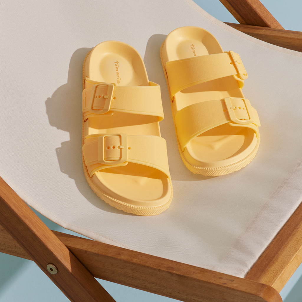Sandales Tamaris jaunes sur une chaise longue blanche en bois.