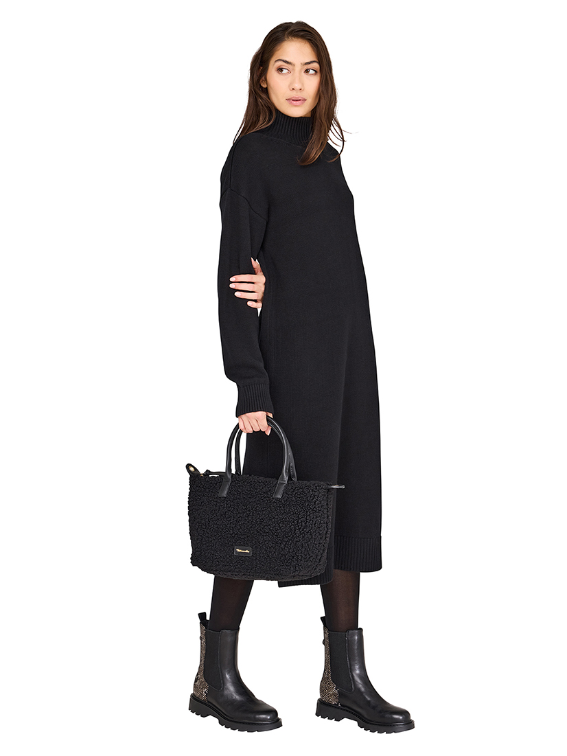 Model in a black knitted dress with a turtleneck, a black handbag and black Chelsea boots with a snake pattern.
