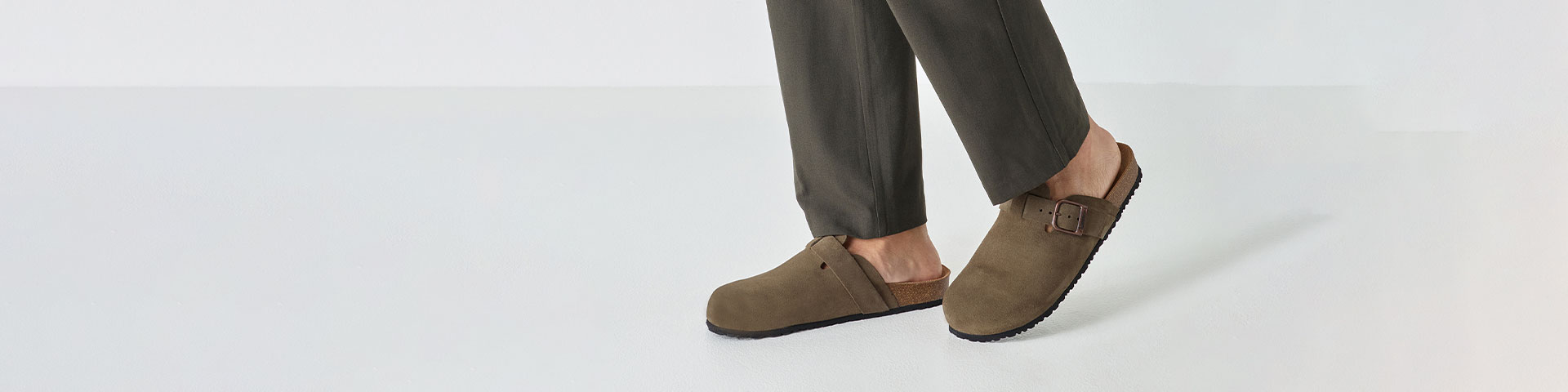 Mules vert olive en cuir nubuck avec boucle r&eacute;glable, port&eacute;es avec un pantalon fonc&eacute; sur fond blanc.