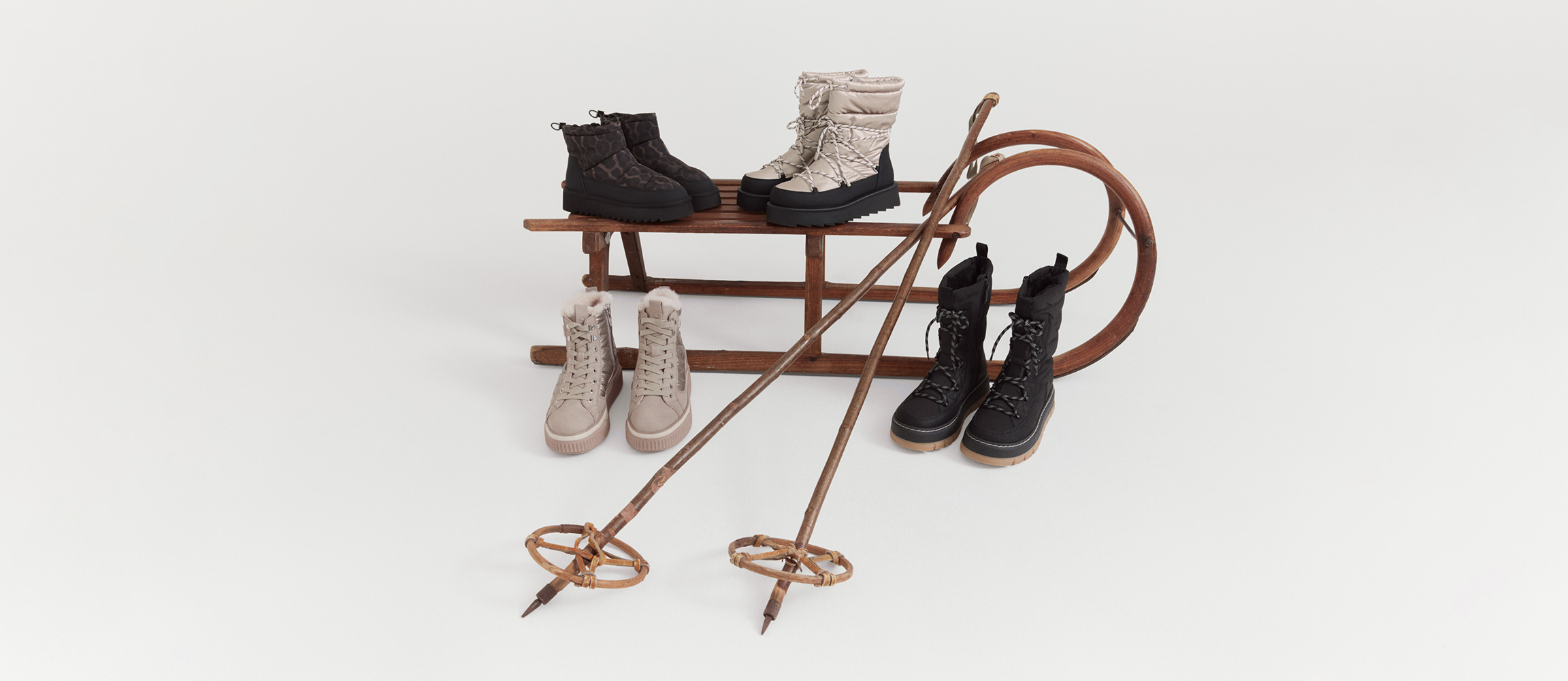 Des chaussures d&rsquo;hiver claires et fonc&eacute;es, dispos&eacute;es sur un tra&icirc;neau en bois devant un fond blanc