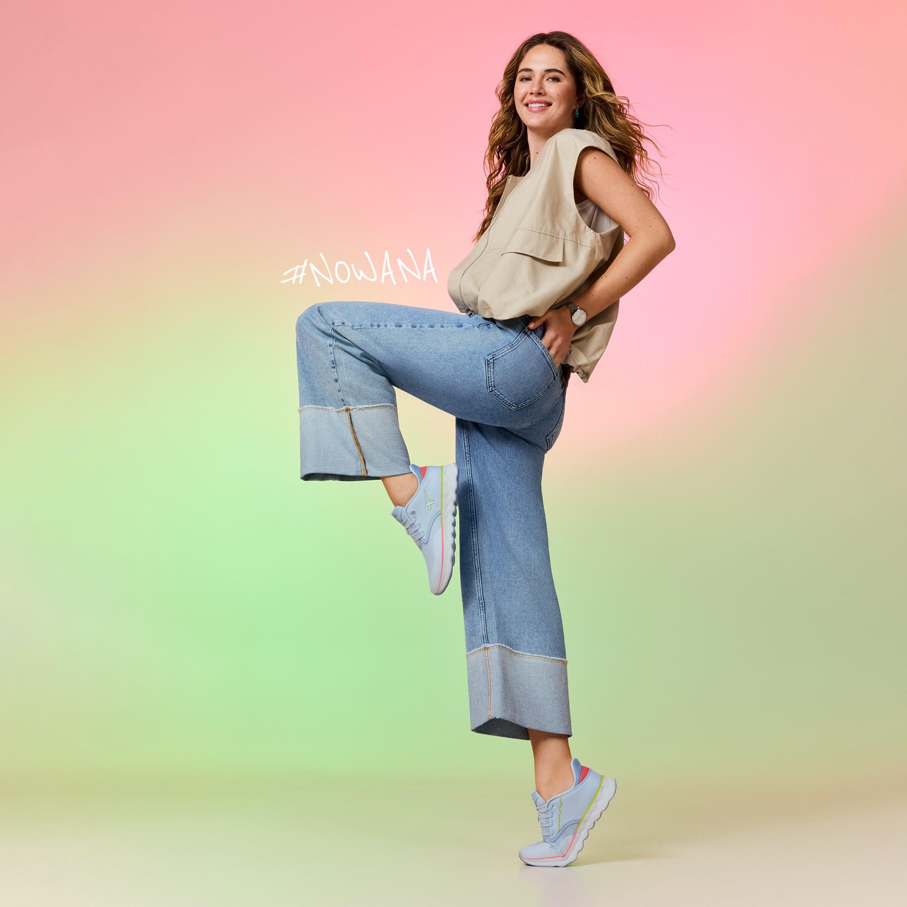 Mannequin en gilet beige et jean pose de mani&egrave;re dynamique devant un fond pastel, portant des sneakers bleues avec des d&eacute;tails roses