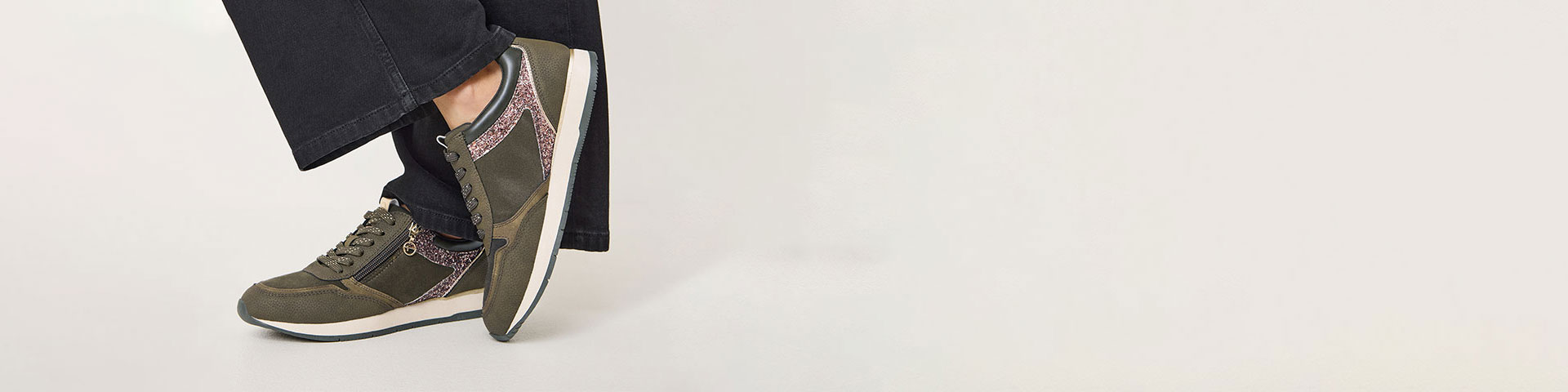 Bruine sportschoenen met witte zolen op voeten met zwarte broek tegen een witte achtergrond