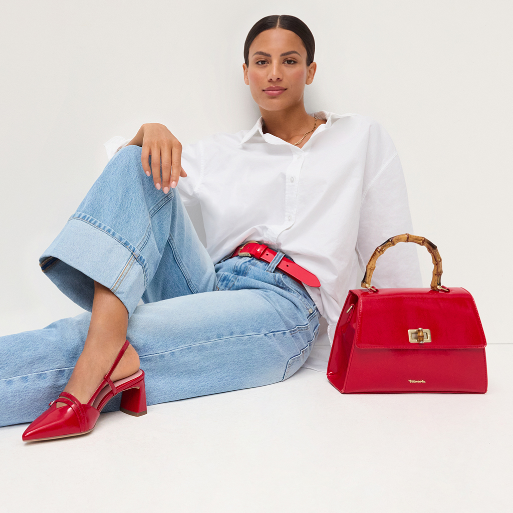 Frau in wei&szlig;er Bluse und Jeans, kombiniert mit roten Accessoires - Handtasche mit Bambusgriff, G&uuml;rtel und spitze Schuhe