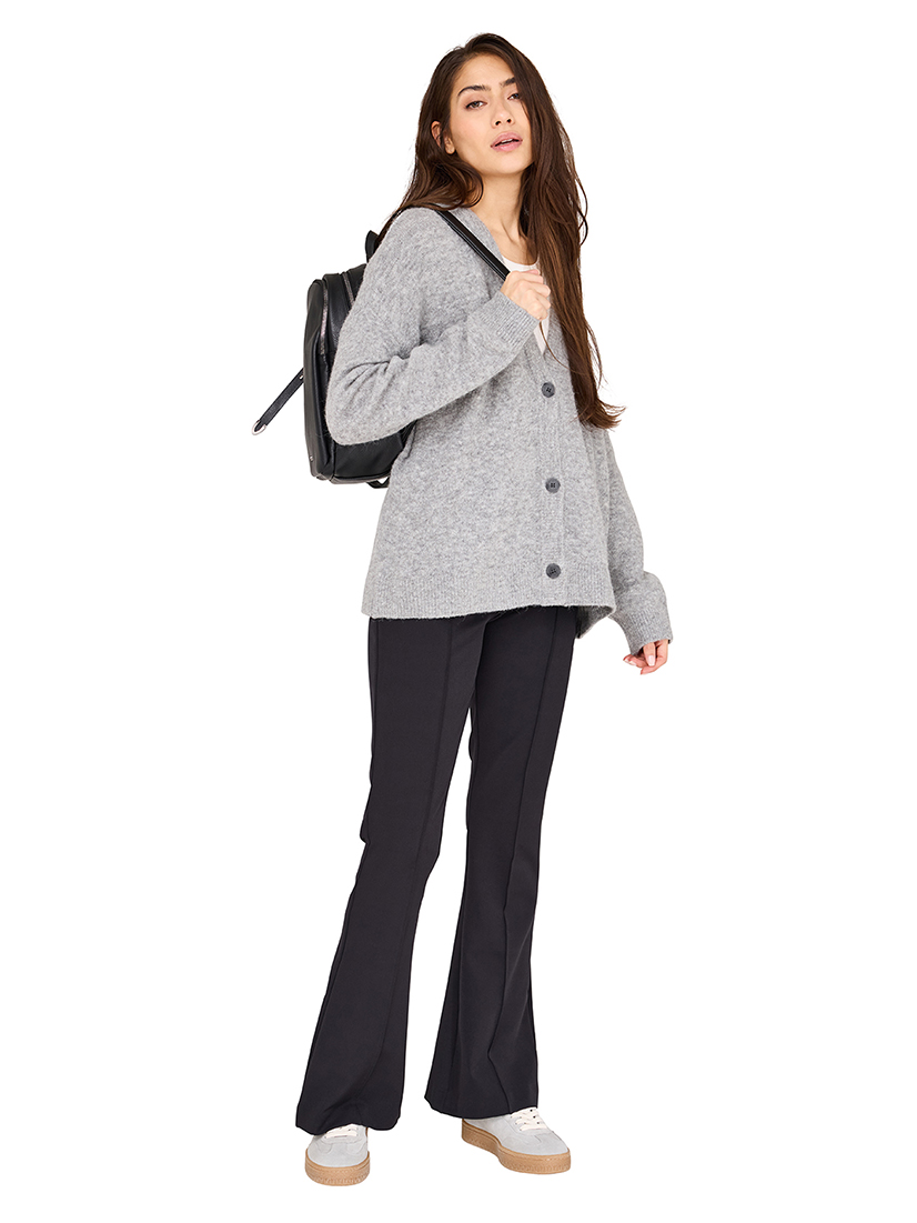 Modell in grauer Strickjacke, schwarzer Hose und Sneakers trägt einen schwarzen Rucksack in lässigem Casual-Look