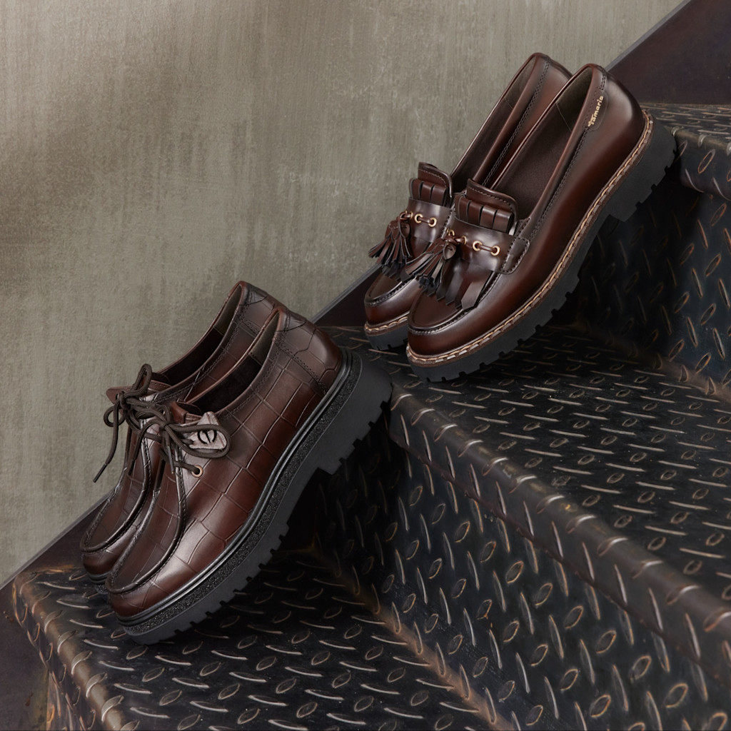 Two brown women's shoes on metal steps: a lace-up shoe with a croc pattern and a loafer with tassels and a platform sole.