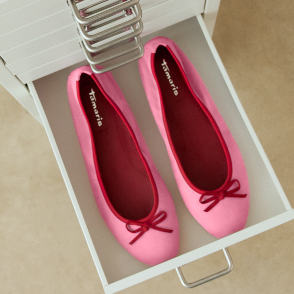 Roze ballerina&rsquo;s met kleine strikjes op een wit schoenenrek.