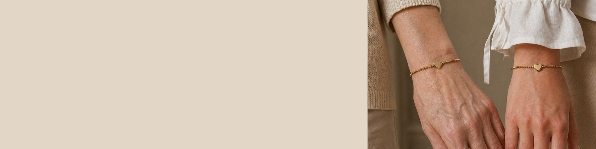 Due mani indossano braccialetti a sfere dorate con ciondolo a forma di cuore. Una persona indossa un maglione beige, l&rsquo;altra una camicetta bianca.