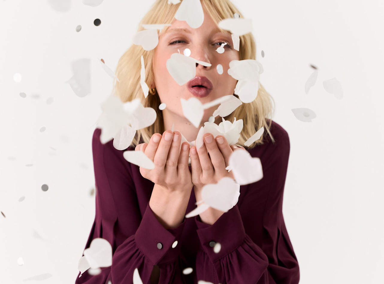 K&uuml;nstlerisches Portr&auml;t mit fliegenden wei&szlig;en Papierbl&uuml;ten, Person in burgunderrotem Oberteil vor hellem Hintergrund