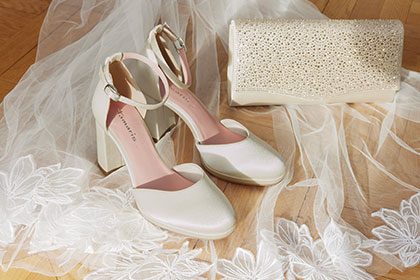 Elegant white bridal shoes surrounded by delicate tulle and lace on a light wooden floor.