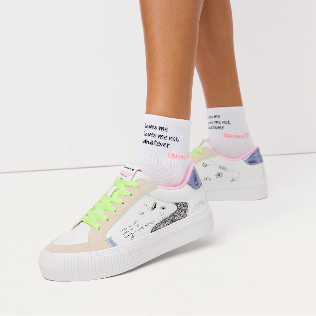 Sneakers bianche con lacci verde neon e calze con scritta, fotografate su sfondo chiaro.