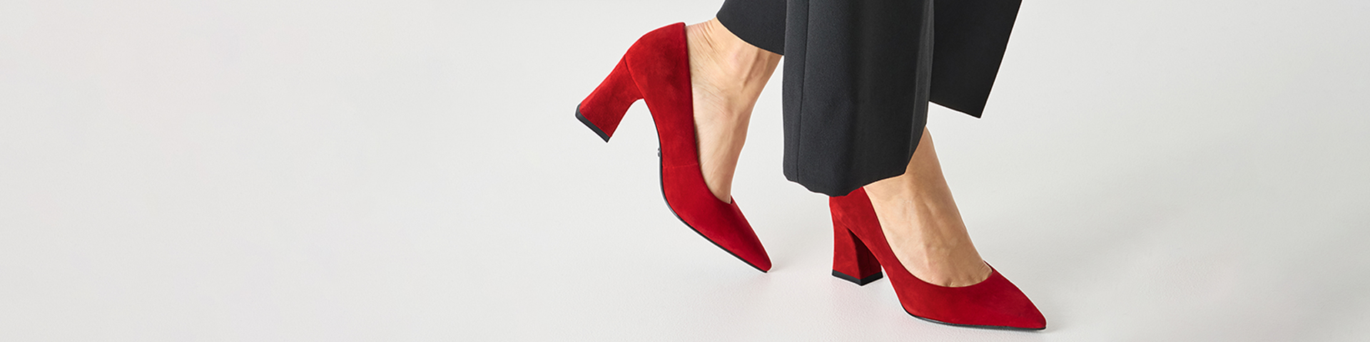 Elegante rode su&egrave;de pumps met blokhak, gedragen met een zwarte broek op een witte achtergrond