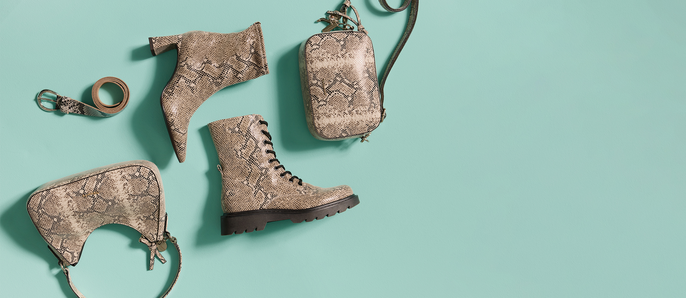 Stiefel mit Schlangenmuster liegen auf t&uuml;rkisfarbenem Hintergrund, k&uuml;nstlerisch arrangiert mit dramatischem Schattenwurf.