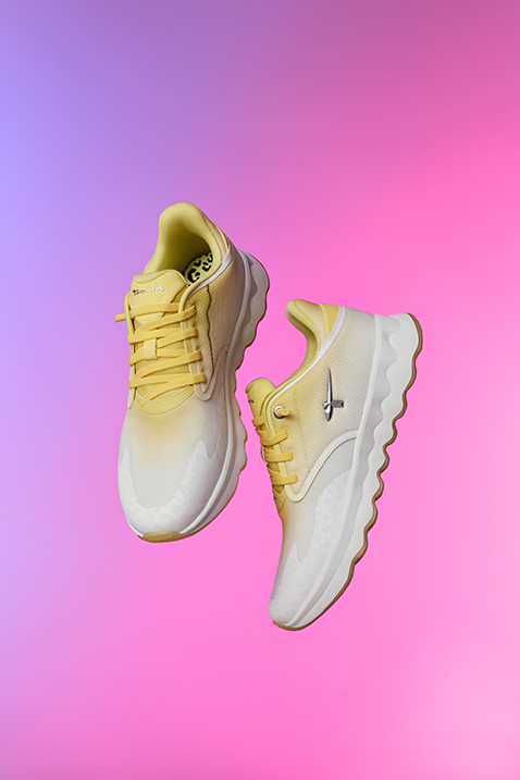 Yellow and white sports shoes with a color gradient float in front of a pink-purple background.