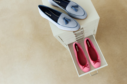 Mehrere Paar rosa und wei&szlig;e Ballerinas in Schuhkartons, ordentlich aufgereiht auf hellem Untergrund.