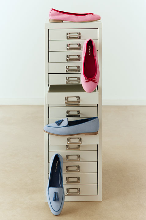 Scarpe da donna colorate in rosa e blu, disposte in modo decorativo accanto a un mobile bianco con cassetti.