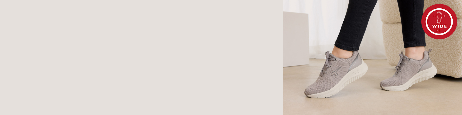 Grey sneakers with mesh upper and white sole, worn with black trousers, with wide-fit logo in the corner