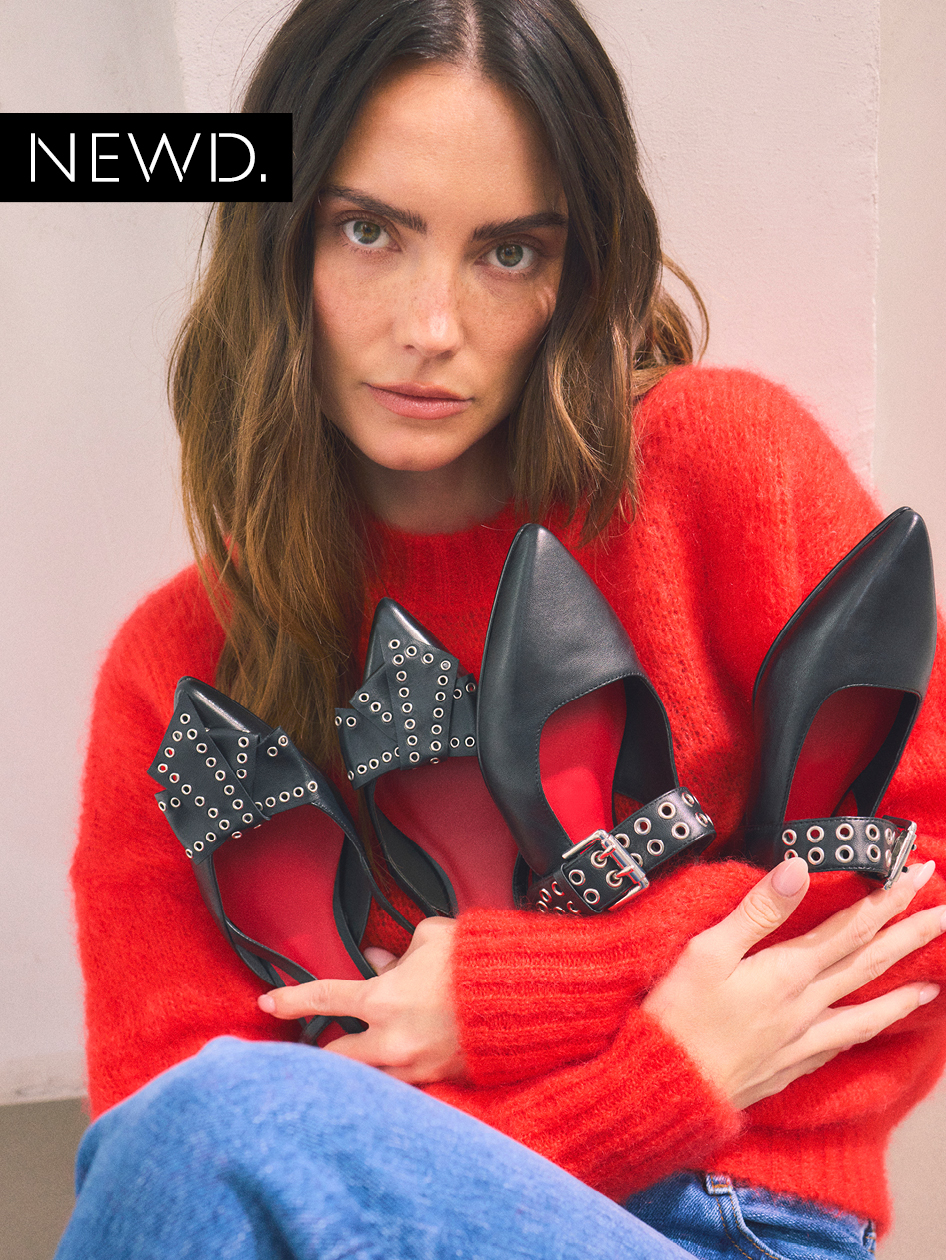 Modewerbung: Frau in rotem Pullover präsentiert schwarze Lederschuhe mit Nietenverzierung, trägt blaue Jeans