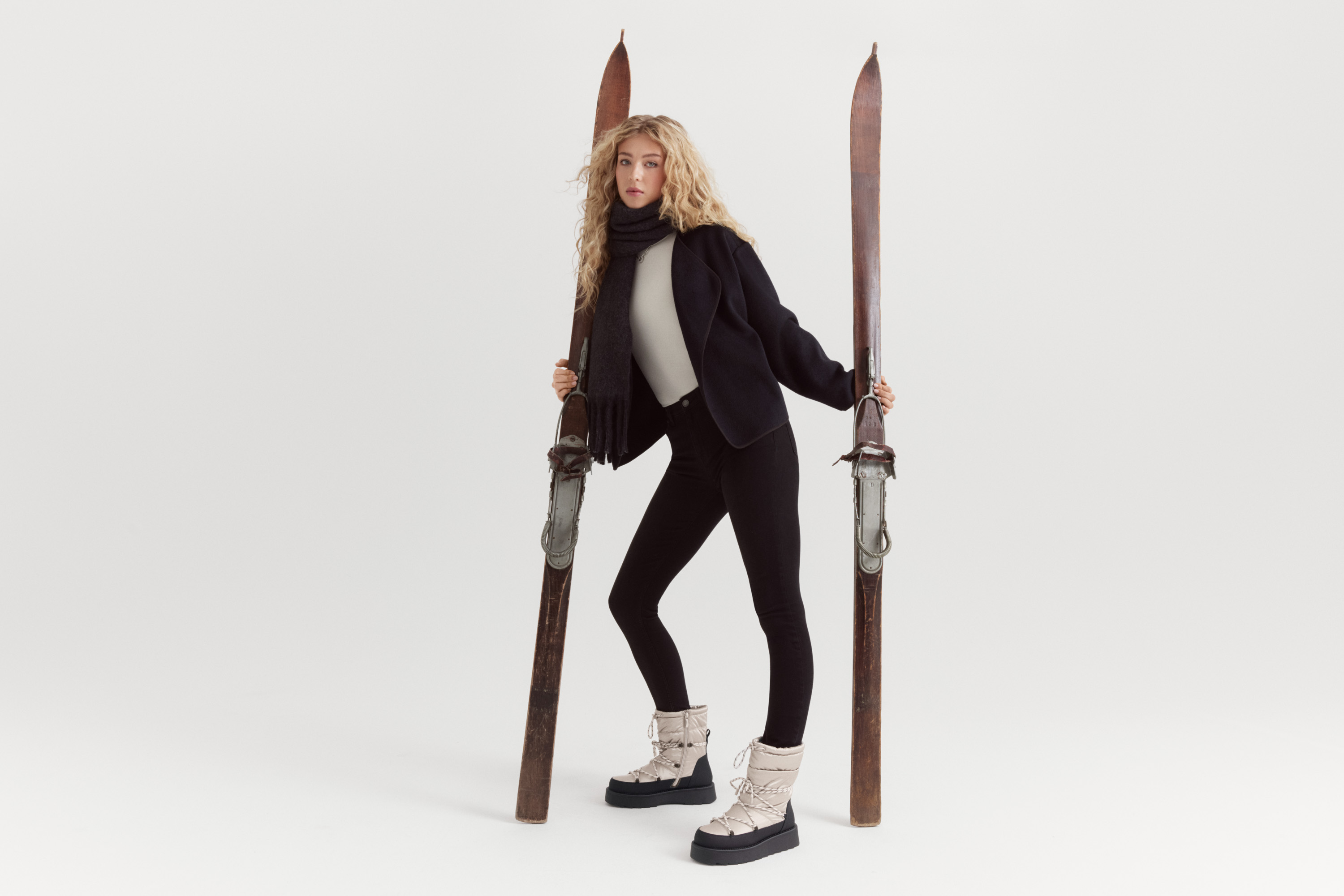 Fashionable winter outfit with a black blazer, turtleneck and leggings, combined with bright platform boots against a white background.