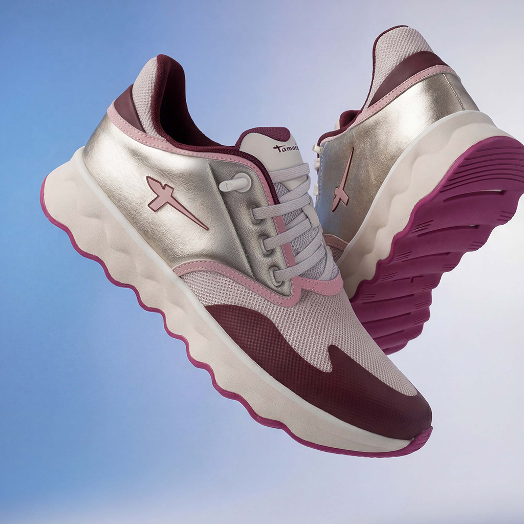 Tamaris‑sneaker in zilver, roze en bordeaux met dikke witte zool en roze loopzool tegen een blauwe achtergrond.