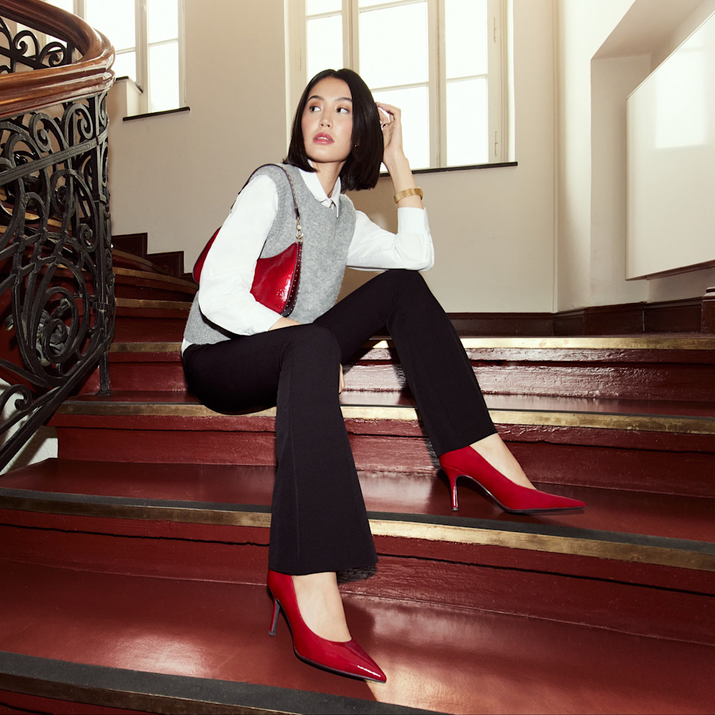 Tenue D'affaires élégante avec gilet gris, chemisier blanc et escarpins rouges sur un escalier en bois historique avec balustrade en fer forgé.