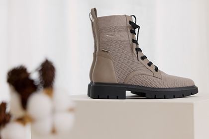 Beige ankle boots with laces and black soles, presented on a white platform.