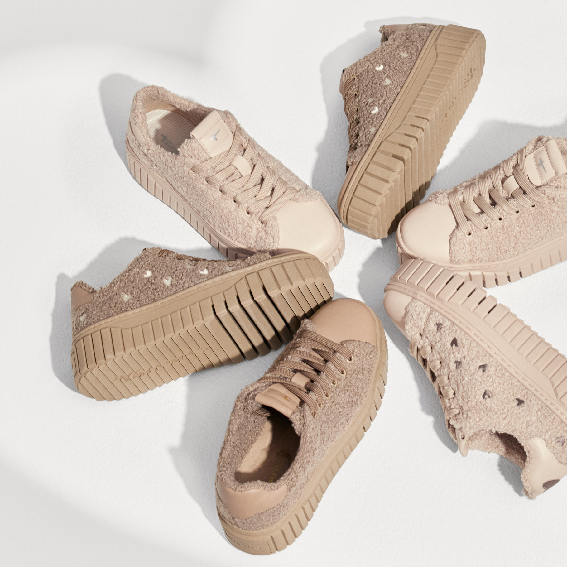 Vier beige Plateau-Sneaker mit Teddy-Textur und dicker Profilsohle, kreisf&ouml;rmig auf wei&szlig;em Hintergrund angeordnet.