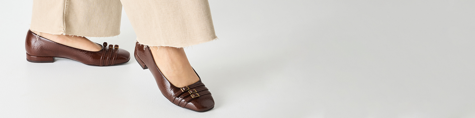 Bruine leren ballerina's met decoratieve bandjes aan de voorkant, gedragen met een lichtgekleurde broek met gerafelde zomen.