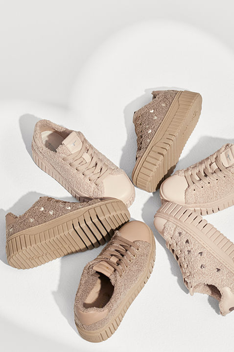 Drei beige Plateau-Sneaker mit Teddy-Textur und dicker Profilsohle, kreisf&ouml;rmig angeordnet auf hellem Hintergrund.