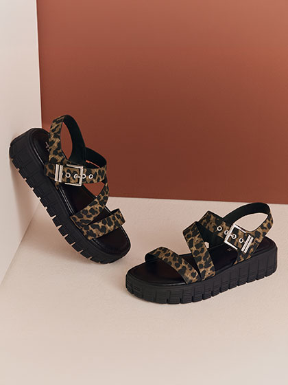 Schwarze Plateau-Sandalen mit Leopardenmuster-Riemen auf beigem Hintergrund mit terrakottafarbener Wand