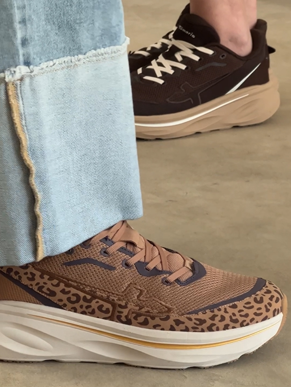 Zwei Personen tragen Tamaris Sneaker: einer mit Leopardenmuster in Braun, einer in Dunkelbraun, kombiniert mit hellblauen Jeans.