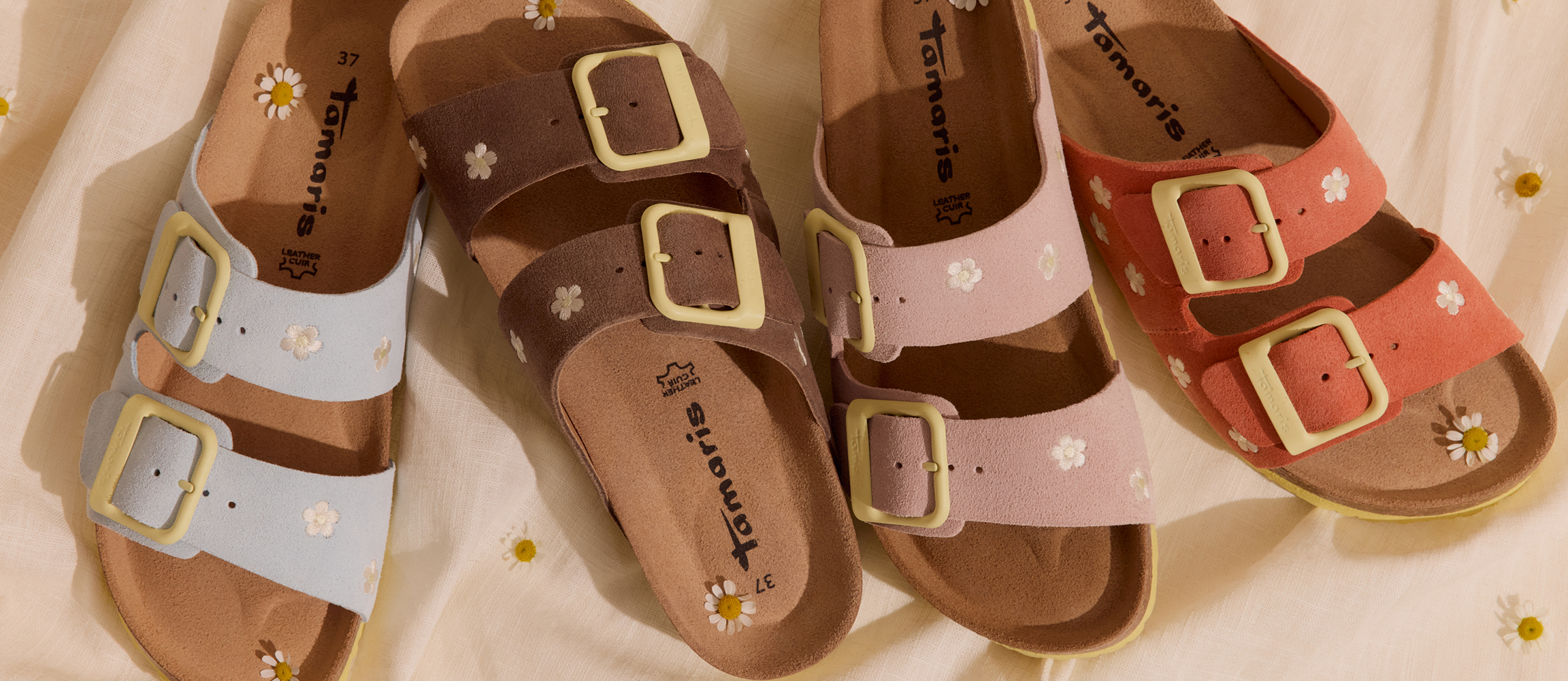 Vier Tamaris-pantoffels met bloemenpatroon op een beige doek.