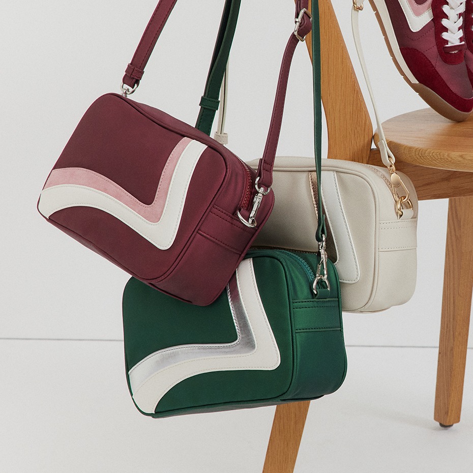 Da una sedia di legno pendono tre borse di colore rosso vino, verde e beige con strisce a V a contrasto.