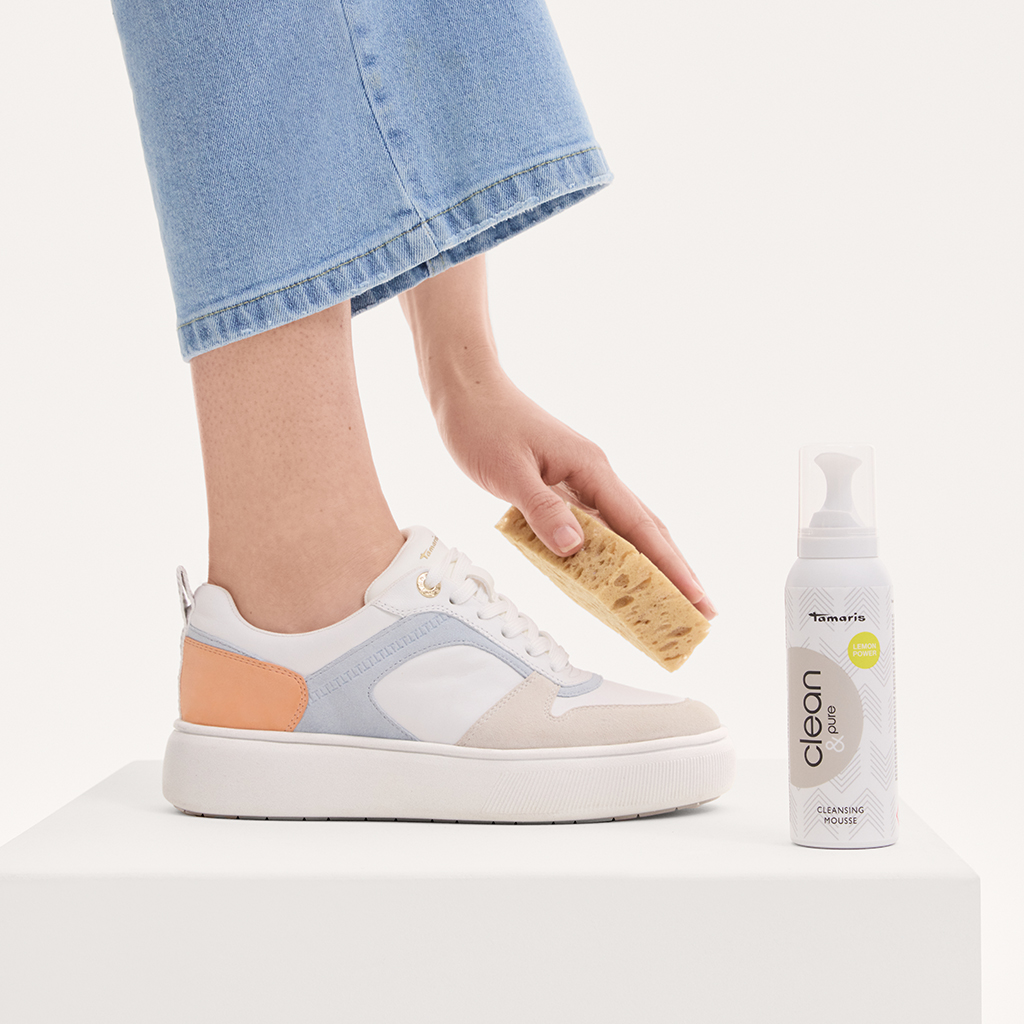 Sneaker-Reinigung mit Bürste und Tamaris Clean Reinigungsschaum, Beine in Jeans und weißen Plateau-Sneakern sichtbar