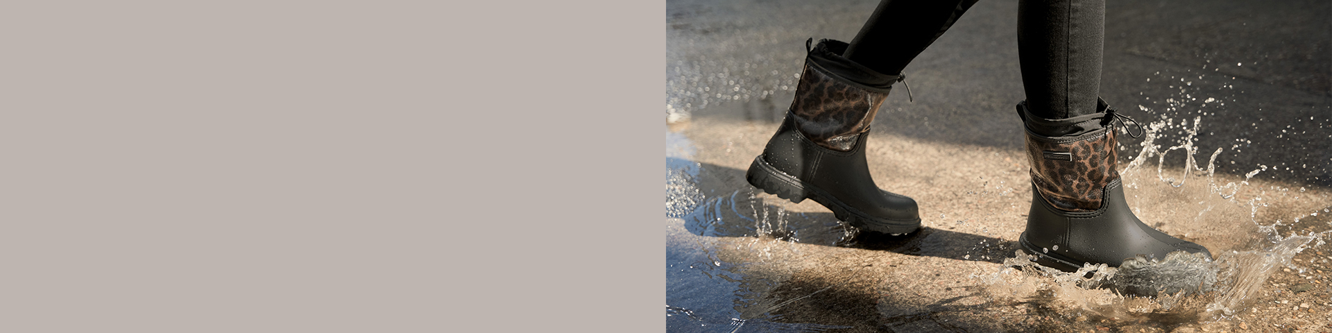 Des bottes en caoutchouc noires avec des détails à motif léopard claquent dans une flaque d'eau et créent des éclaboussures d'eau sur un sol mouillé.