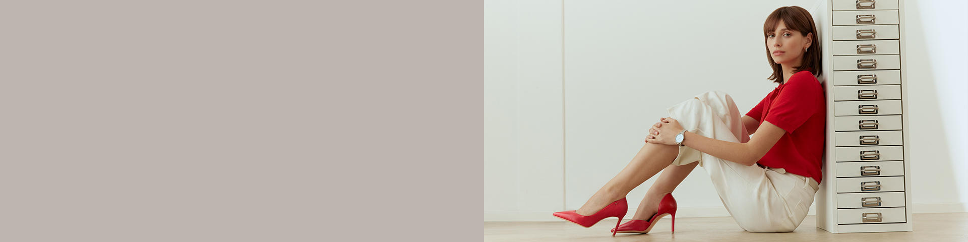 Woman sits on the floor with bent legs, wearing red pumps.