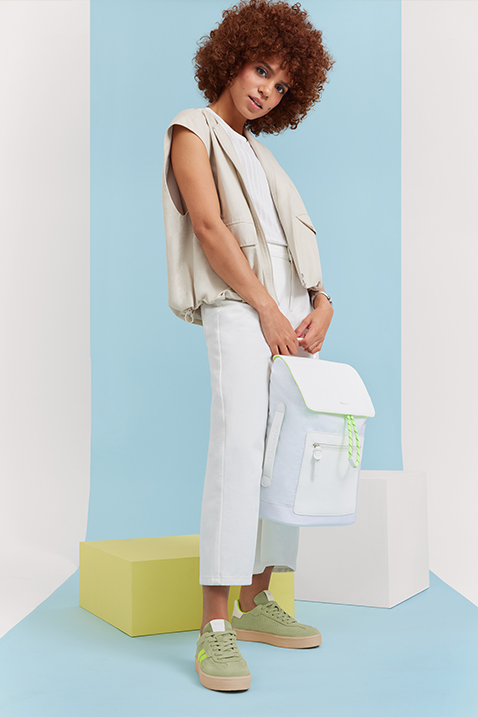 Model in white summer outfit with curly hair poses against a light blue backdrop, wearing mint green sneakers.