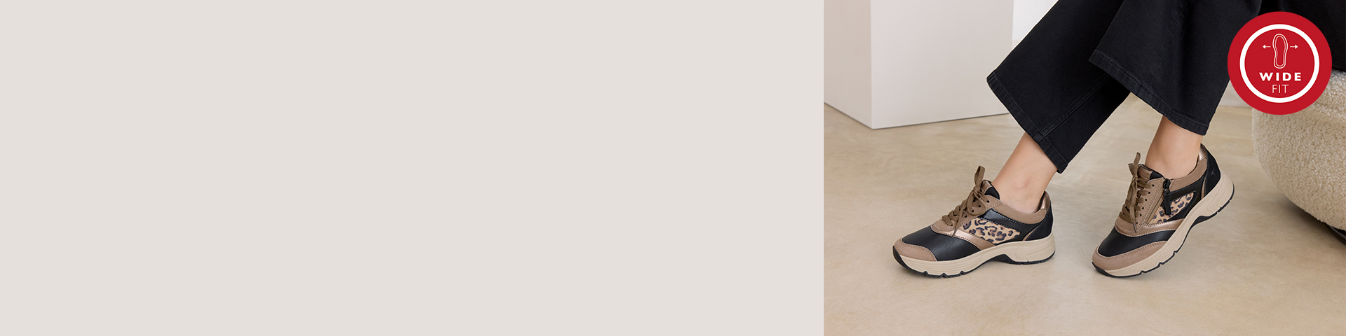 Sportieve sportschoenen in beige en zwart met details van luipaardprint, gedragen met een zwarte broek op een beige basis en een rood wide-fit logo rechtsboven