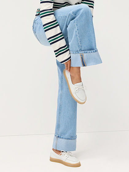 Benen in wijde jeans met omgeslagen zoom en witte bootschoenen.