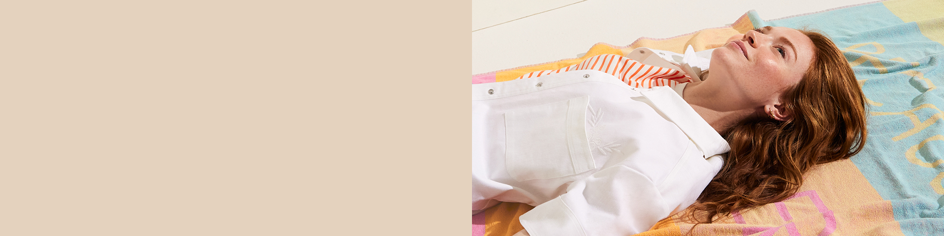 Een ontspannen persoon in een witte blouse ligt op kleurrijk textiel en geniet van een rustig moment in een warme sfeer.