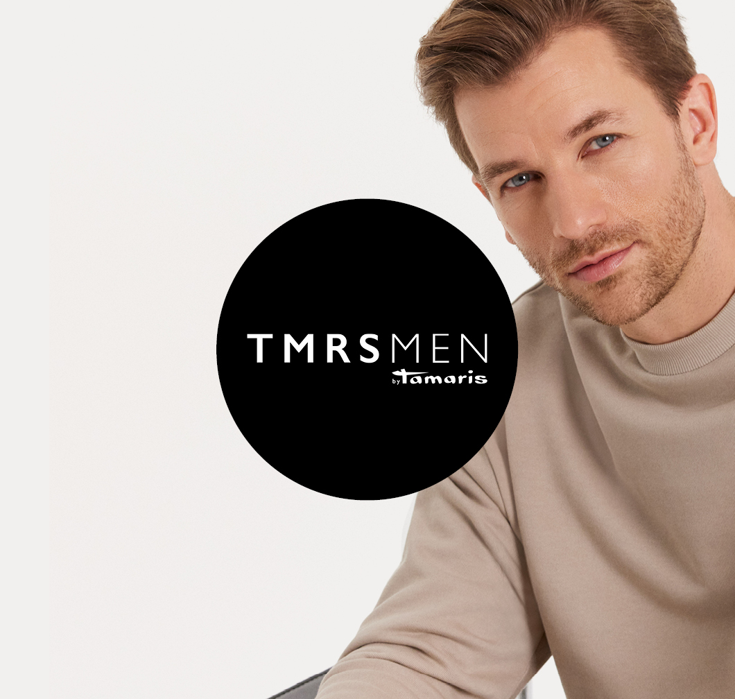 Man in a beige jumper with a TMRS MEN by Tamaris logo on a black circle in the foreground.