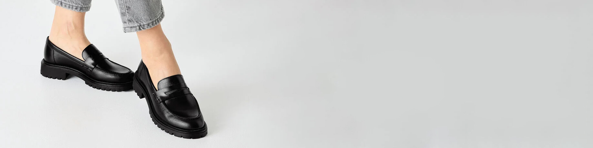 Black loafers with sturdy tread sole, worn with light grey jeans against a white background