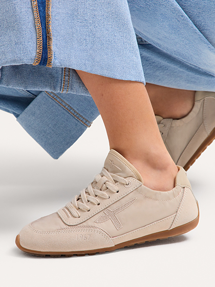 Close-up of beige sneakers paired with light blue jeans against a white background.